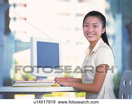 Stock Photo - Image of a Young Adult Woman Using a Computer, Smiling, Looking Sideways, Side View, Differential Focus. Fotosearch