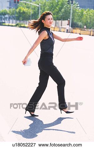 Stock Photo - Image of a Young Adult Woman Walking Outdoors, Smiling, Her Hair Waving in the Air, Side View. Fotosearch