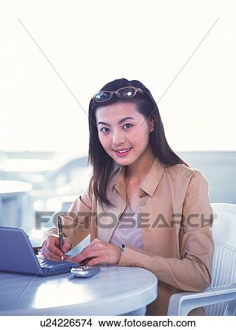 Image of a Young Businesswoman Working at a Desk, Smiling, Looking at Camera, Side View View Large Photo Image Picture - Image of a Young Businesswoman Working at a Desk, Smiling, Looking at Camera, Side View. Fotosearch
