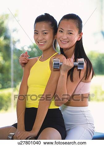 Image of Two Young Adult Woman Sitting Together, Smiling, One Holding a Weight, Looking at Camera, Front View, Differential Focus View Large Photo Image Stock Image - Image of Two Young Adult Woman Sitting Together, Smiling, One Holding a Weight, Looking at Camera, Front View, Differential Focus . Fotosearch