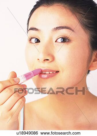 Stock Photograph - Japanese woman applying lipstick, looking at camera. Fotosearch