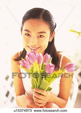 Stock Image - Japanese woman holding a bunch of tulips, smiling . Fotosearch