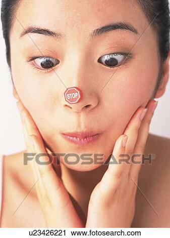 Stock Image - Japanese woman looking down stop sign sticking on her nose. Fotosearch