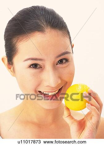 Stock Image - Japanese woman smiling and holding a lemon. Fotosearch