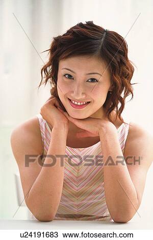 Stock Image - Portrait of Japanese woman putting elbows on table, smiling. Fotosearch