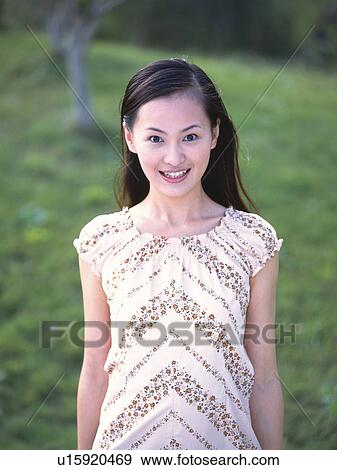 Stock Photo - Portrait of Japanese woman smiling in green field. Fotosearch