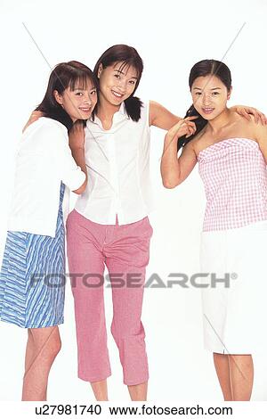 Stock Image - Portrait of three women smiling and standing, one putting arms around the others. Fotosearch