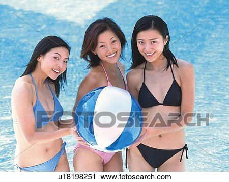 Stock Image - Three women holding a beach ball, smiling in the pool . Fotosearch