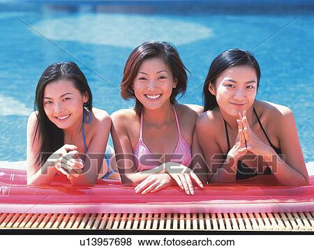 Stock Photo - Three women putting elbows on pool raft, smiling at the side of the pool . Fotosearch