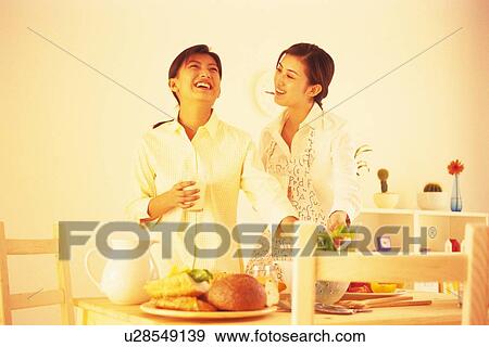 Stock Photo - Two woman talking and laughing at kitchen. Fotosearch