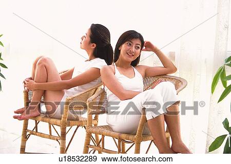 Stock Photo - Two women sitting on chair, back to back. Fotosearch