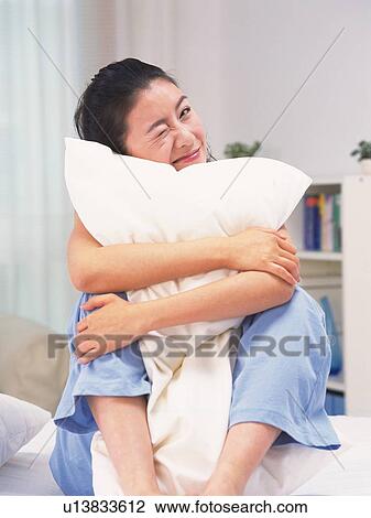 Stock Image - Woman clutching a pillow to chest on bed, winking. Fotosearch