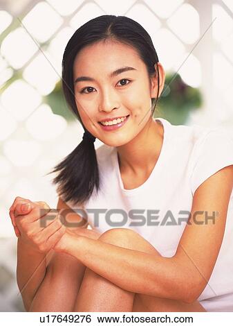 Stock Photograph - Woman folding hands and clutching her knees to chest, smiling. Fotosearch