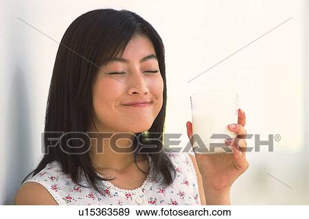 Stock Photo - Woman holding a glass of milk, closing eyes. Fotosearch
