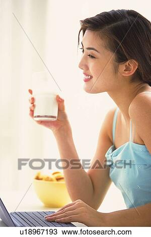Woman holding a glass of milk, using a laptop View Large Photo Image Stock Image - Woman holding a glass of milk, using a laptop. Fotosearch