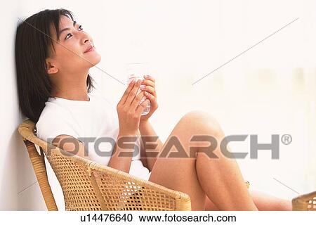 Stock Image - Woman holding a plastic bottle, sitting down on chair. Fotosearch