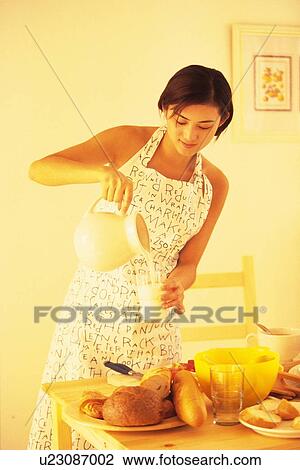 Stock Image - Woman pouring glass of milk from jug at kitchen. Fotosearch