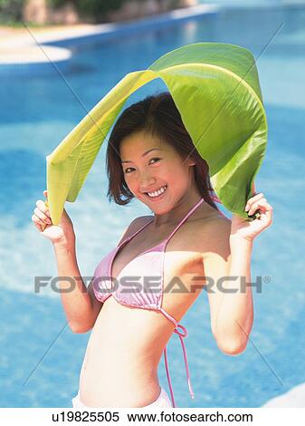 Stock Photography - Woman wearing bikini, protecting from the sun by big leaf. Fotosearch