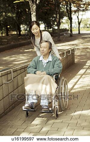 Stock Photo - Daughter pushing father in wheelchair . Fotosearch