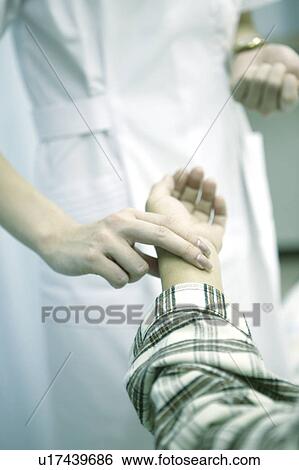 Stock Photograph - Nurse takes the pulse of a patient lying in a hospital bed . Fotosearch