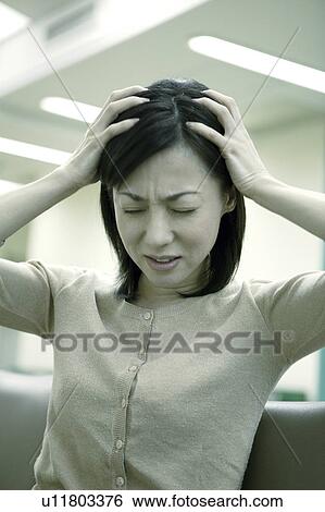 Stock Photograph - Woman holds her head as if suffering from a headache . Fotosearch