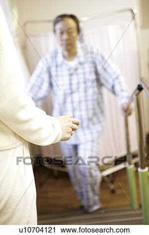 Stock Image - Young nurse assisting beside man using orthopedic walker . Fotosearch
