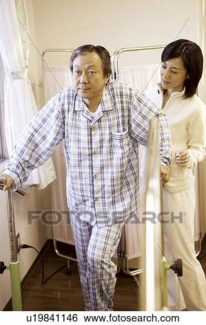 Stock Photograph - Young nurse assisting beside man using orthopedic walker . Fotosearch