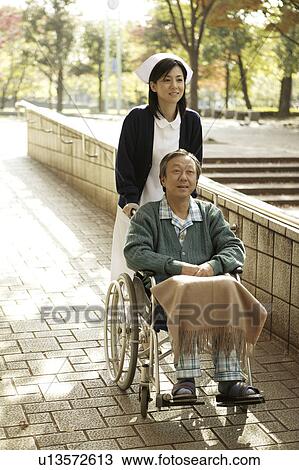 Stock Image - Young nurse pushing man patient in wheelchair . Fotosearch