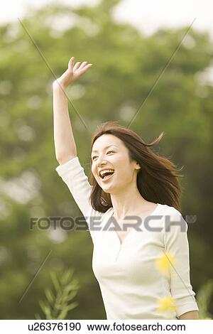 Stock Image - Photography of a mid adult woman in the field waving hand, Differential Focus. Fotosearch