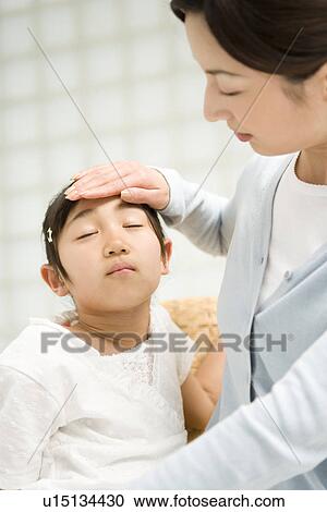 Stock Image - Photography of a mother checking daughter's temperature, Low Angle View. Fotosearch