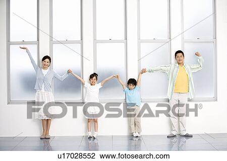 Stock Image - Photography of parents and children holding hands and standing by the windows, Front View. Fotosearch