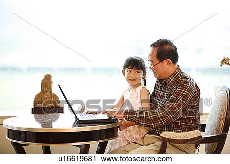 Stock Image - A small girl learning on laptop through her grandfather.. Fotosearch