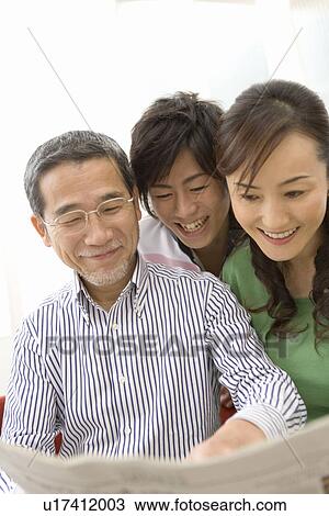 Stock Image - A Family Smiling and Reading a Newspaper Together, Front View. Fotosearch
