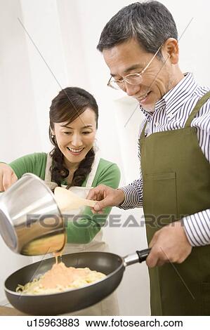 Stock Image - A Mature Adult Couple Cooking Together, Front View, Side View. Fotosearch