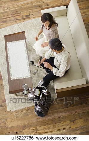 Stock Photograph - A Mature Adult Couple on a Sofa Looking at a Golf Club Together, High Angle View. Fotosearch