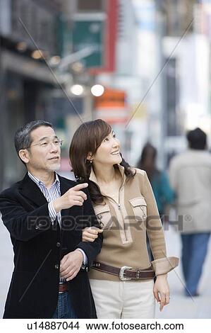 A Mature Adult Couple Smiling and Pointing Away on a Street, Side View, Differential Focus View Large Photo Image Picture - A Mature Adult Couple Smiling and Pointing Away on a Street, Side View, Differential Focus. Fotosearch