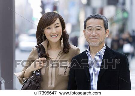 Stock Photo - A Mature Adult Couple Smiling on a Street, Front View, Differential Focus. Fotosearch