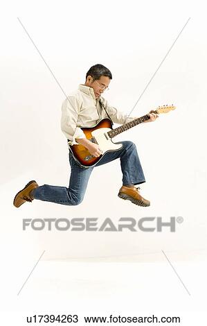 Stock Image - A Mature Adult Man Jumping and Playing a Guitar, Side View. Fotosearch
