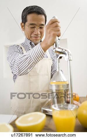 Stock Image - A Mature Adult Man Making Grapefruit Juice, Front View, Differential Focus. Fotosearch