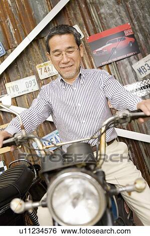 Stock Photograph - A Mature Adult Man on a Motorcycle, Front View, Low Angle View. Fotosearch