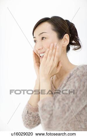 Stock Image - A Mature Adult Woman Moisturising Her Face with Hands, Side View, Low Angle View. Fotosearch