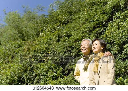 Stock Image - A Mature Couple Nestling Close to Each Other and Looking Away, Waist Up, Low Angle View. Fotosearch