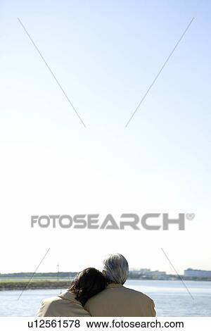 Stock Photo - A Mature Couple Nestling Close to Each Other on the Seashore, Rear View, Head and Shoulder, Copy Space. Fotosearch