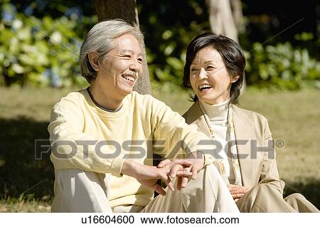 Stock Image - A Mature Couple Sitting on the Ground and Talking, Front View, Three Quarter Length. Fotosearch