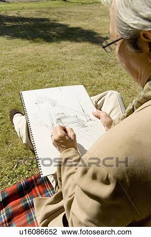 Stock Image - A Mature Man Sketching on the Lawn, Rear View, High Angle View. Fotosearch
