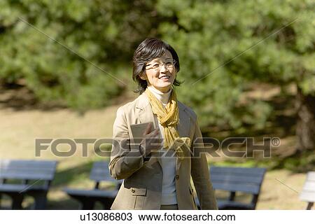 Stock Image - A Mature Woman Holding a Book and Walking, Front View, Waist Up. Fotosearch