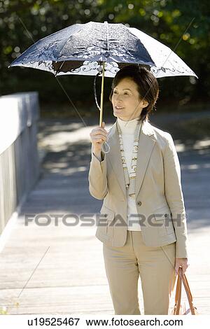 Stock Photo - A Mature Woman Putting Up a Parasol, Front View, Three Quarter Length. Fotosearch