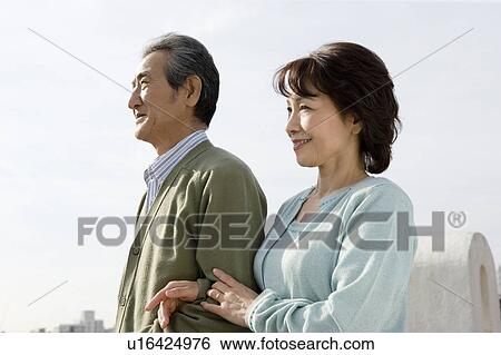 Stock Photograph - A Senior Adult Couple Looking Away Under the Sky, Side View. Fotosearch