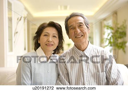 Stock Image - A Senior Adult Couple Smiling at Camera in a Room, Front View, Differential Focus. Fotosearch