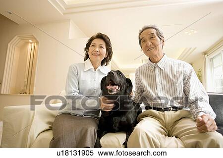 Stock Photography - A Senior Adult Couple Smiling with a Dog in a Living Room, Low Angle View. Fotosearch